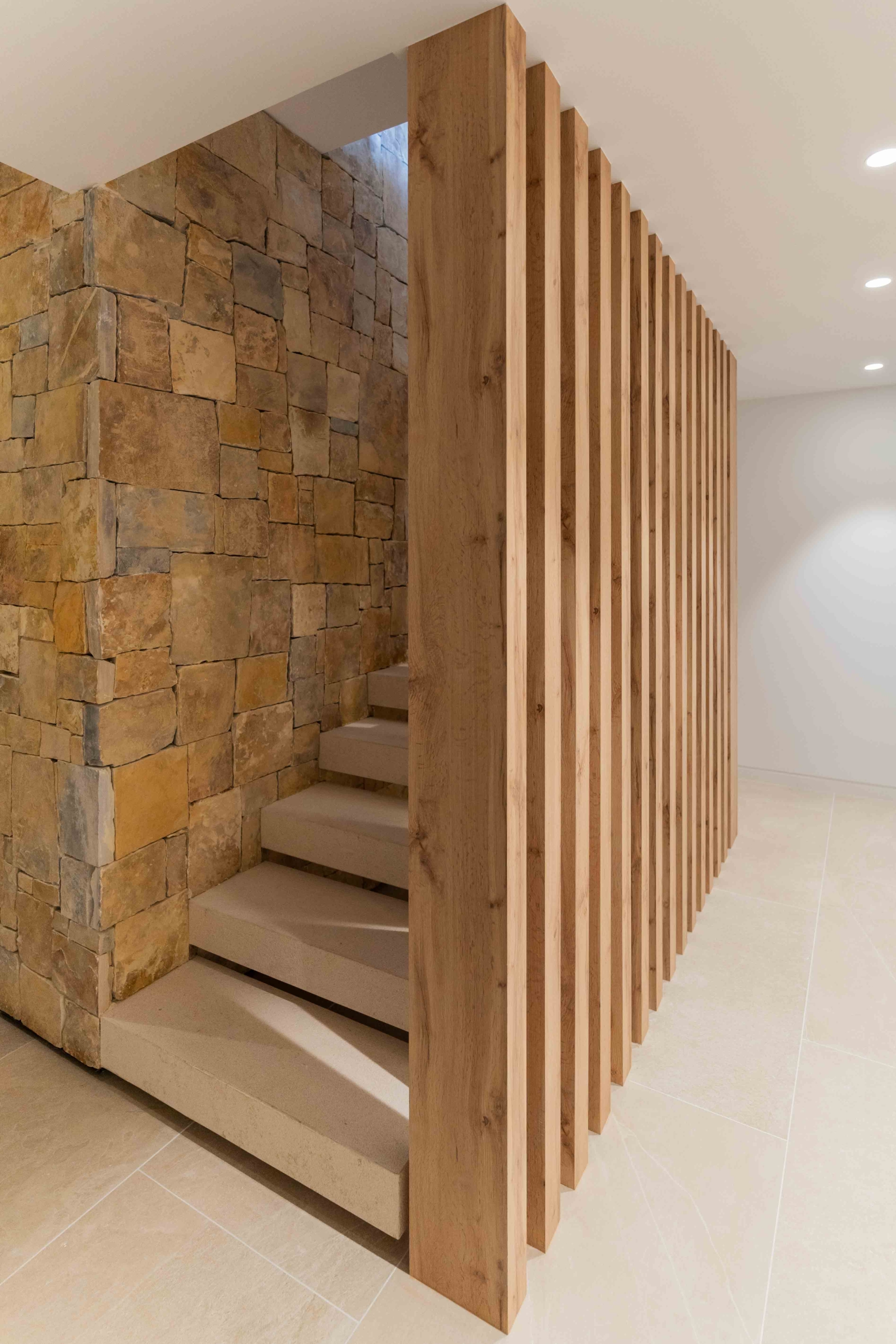 Escaleras interiores vivienda con muro de piedra natural y listones de madera tecnológica